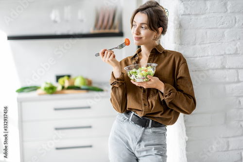 Portrait of a young and cheerful woman eating healthy salad on the kitchen at home. Healthy eating, wellbeing and lifestyle concept