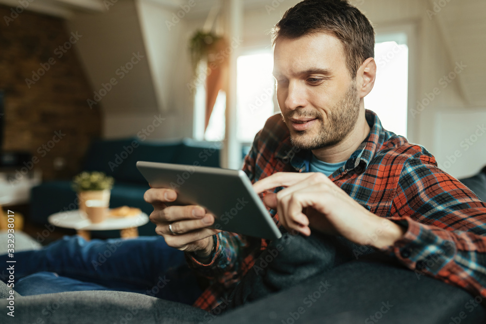 Young smiling man using touchpad while relaxing at home. Young smiling man using touchpad while relaxing at home.