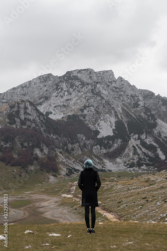 A young woman with blue hair in a black coat walks on the mountainside