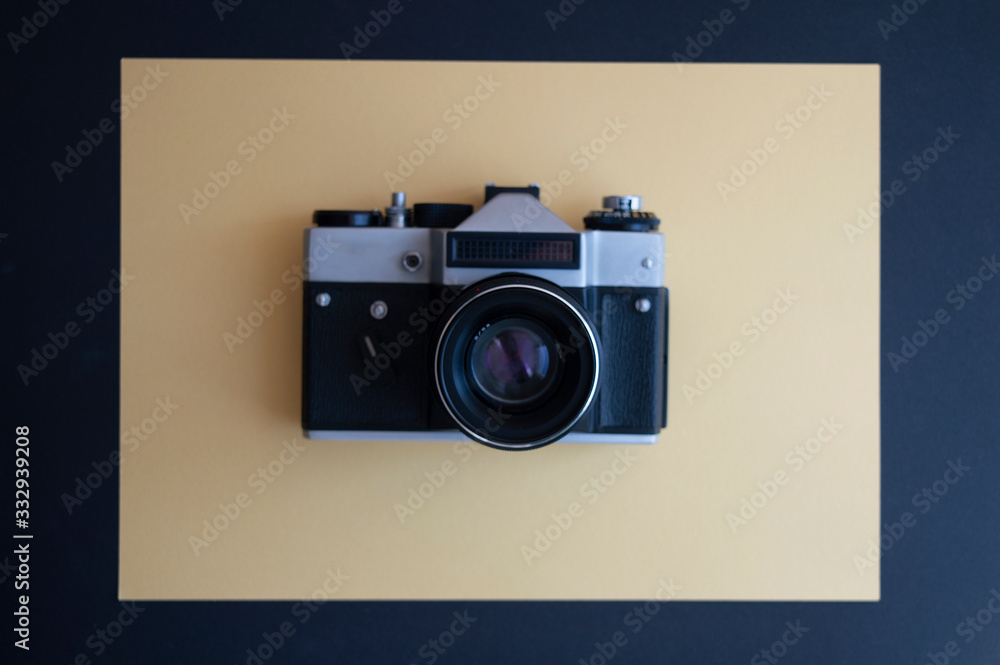 Fototapeta premium View from the top on vintage film photo camera on the dark and yellow background. Metal silver and plastic black frame with lens