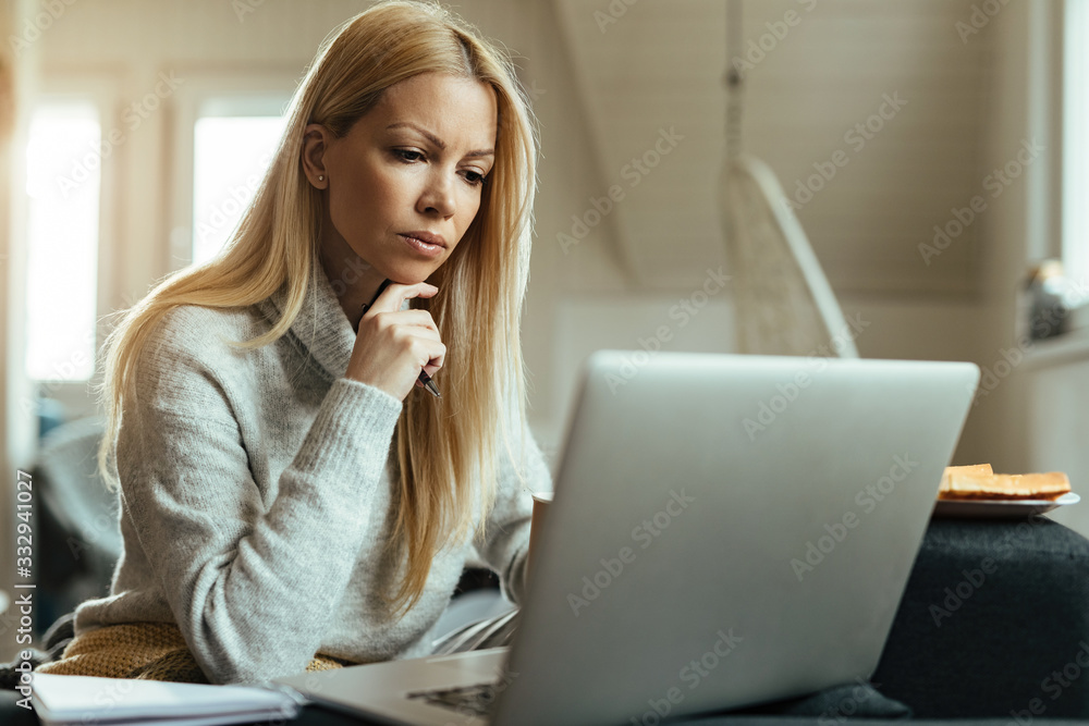 Pensive woman reading an e-mail while working on laptop at home. Pensive woman reading an e-mail while working on laptop at home.