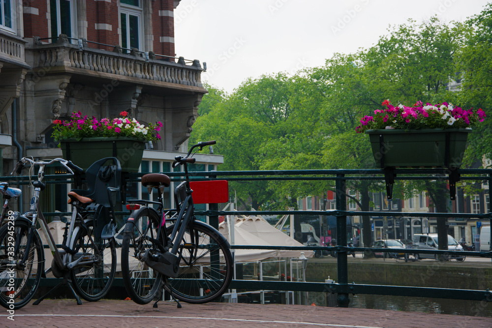 Cityscape of Amsterdam. Bicycle and flowers. Handrail of bridge over canal. Tourism in Europe.