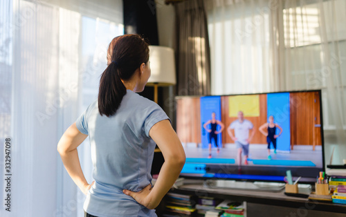 Fototapeta Naklejka Na Ścianę i Meble -  Video streaming Stay home.home fitness workout class live streaming online.Asian woman doing strength training cardio aerobic dance exercises watching videos on a smart tv in the living room at home.