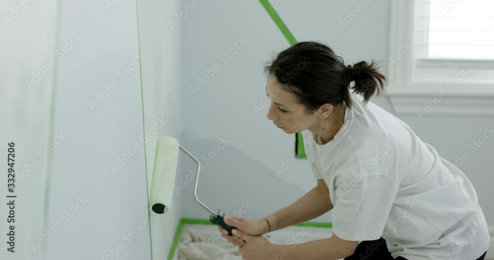 Woman painting bedroom on knees with paint roller - slow motion Woman painting bedroom on knees with paint roller - slow motion