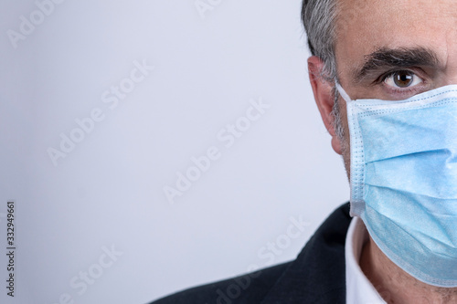 Ritratto di uomo di mezza età che indossa una mascherina chirurgica azzurra isolato su sfondo chiaro neutro photo