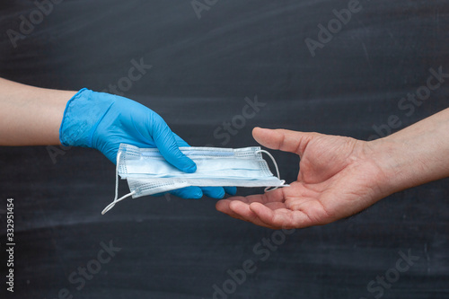 Glove hand gives a medical face mask to hand another person to protect against viruses during an epidemic. Chalk Board in the background