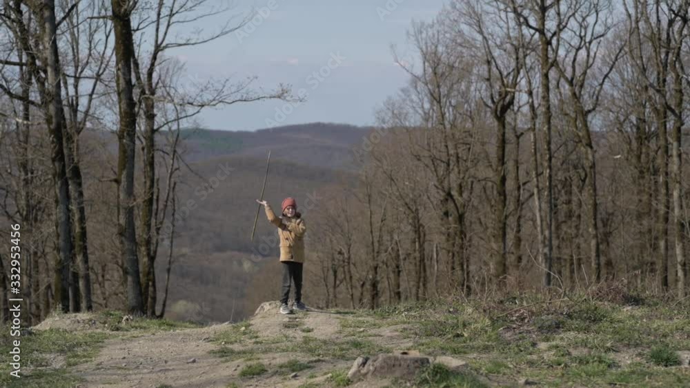 A boy in a yellow jacket twists a stick in the spring forest like a ninja A boy in a yellow jacket twists a stick in the spring forest like a ninja