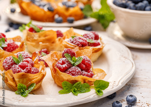 Phyllo cups with Mascarpone cheese filling topped with fresh raspberries and mint on a white plate. Delicious filo pastry dessert