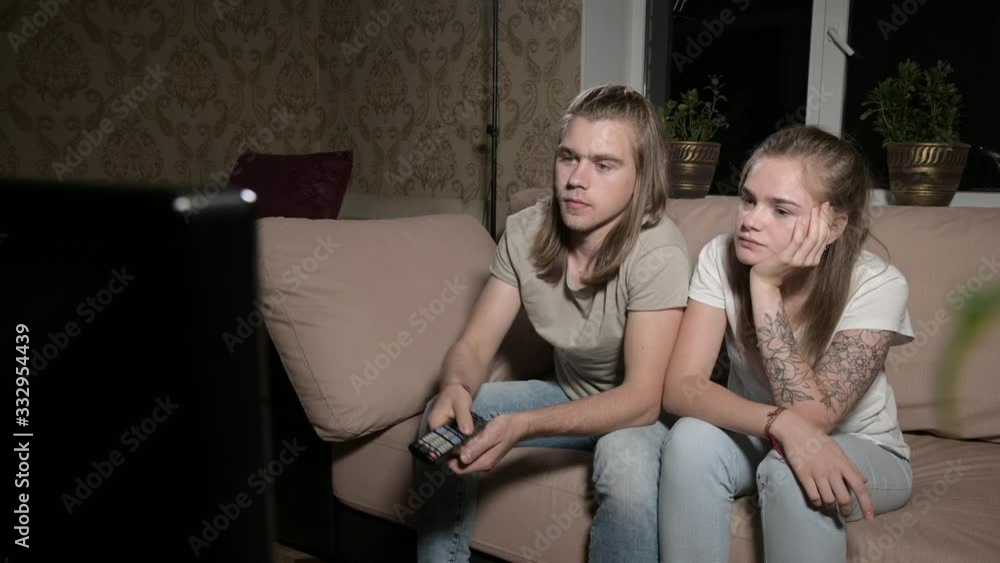 Young couple is watching tv. Man switches channels, woman selects control. Young couple is watching tv. Man switches channels, woman selects control.