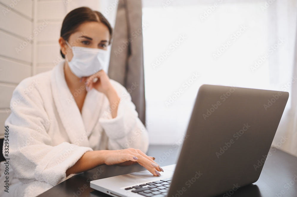 Sick woman in face medical mask working on a laptop during home quarantine isolation COVID-19 pandemic Corona virus. Distance online work from home concept. Coronavirus viral infection symptoms Sick woman in face medical mask working on a laptop during home quarantine isolation COVID-19 pandemic Corona virus. Distance online work from home concept. Coronavirus viral infection symptoms
