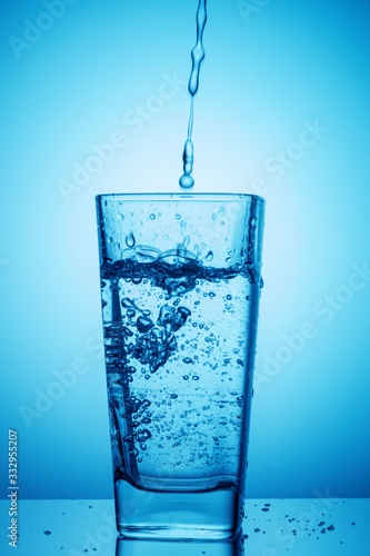 Pouring water into a glass on a blue background. Healthy and green food concept.