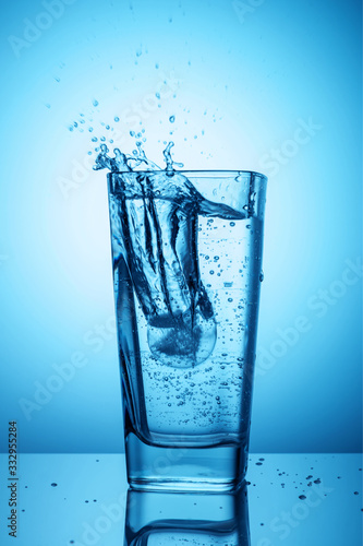 Splashes of clean transparent drinking water in a glass on a blue background