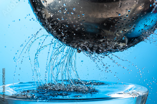 many trickles and drops of water through holes in a meialic colander on a blue background