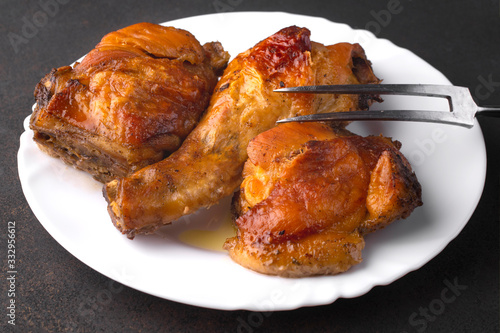 Roasted chicken legs and meat fork on a white plate.