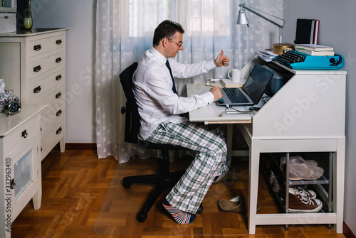 Man working from home with laptop wearing shirt, tie and pajama pants photo