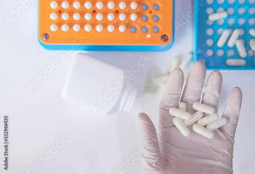 White pill capsules in hand wearing white medical gloves