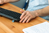 Wooden table with black wireless keyboard, male hands and a notebook. Selective focus