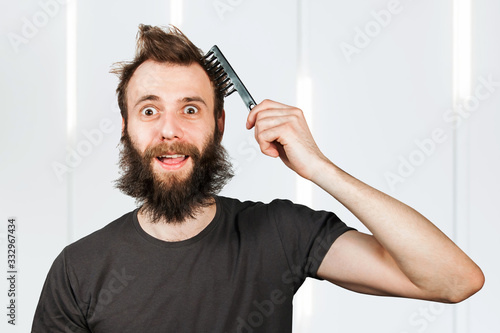 Young bearded overgrown man holding comb and combing his hair. For barbershop.