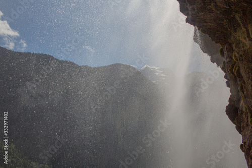 Alps mountain peaks through sunlit water veil, inside the Staubbach waterfall