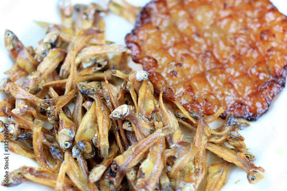 Fried giant catfish and pile of Deep fried small fishes (Minnow fish) Traditional Thai recipes in white dish on rustic wood background. popular in Thailand, important export product of Thailand. Fried giant catfish and pile of Deep fried small fishes (Minnow fish) Traditional Thai recipes in white dish on rustic wood background. popular in Thailand, important export product of Thailand.