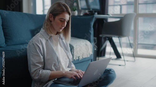 Young woman sitting on the floor near couch work on freelance typing email on laptop focused girl use computer for study online female user busy on distance internet job at home slow motion