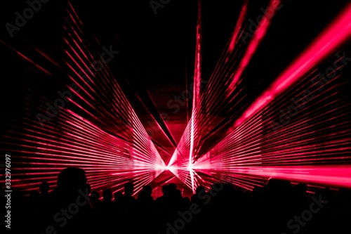 Red laser show nightlife club stage with party people crowd. Luxury entertainment with audience silhouettes in nightclub event, festival or New Year's Eve. Beams and rays shining colorful lights