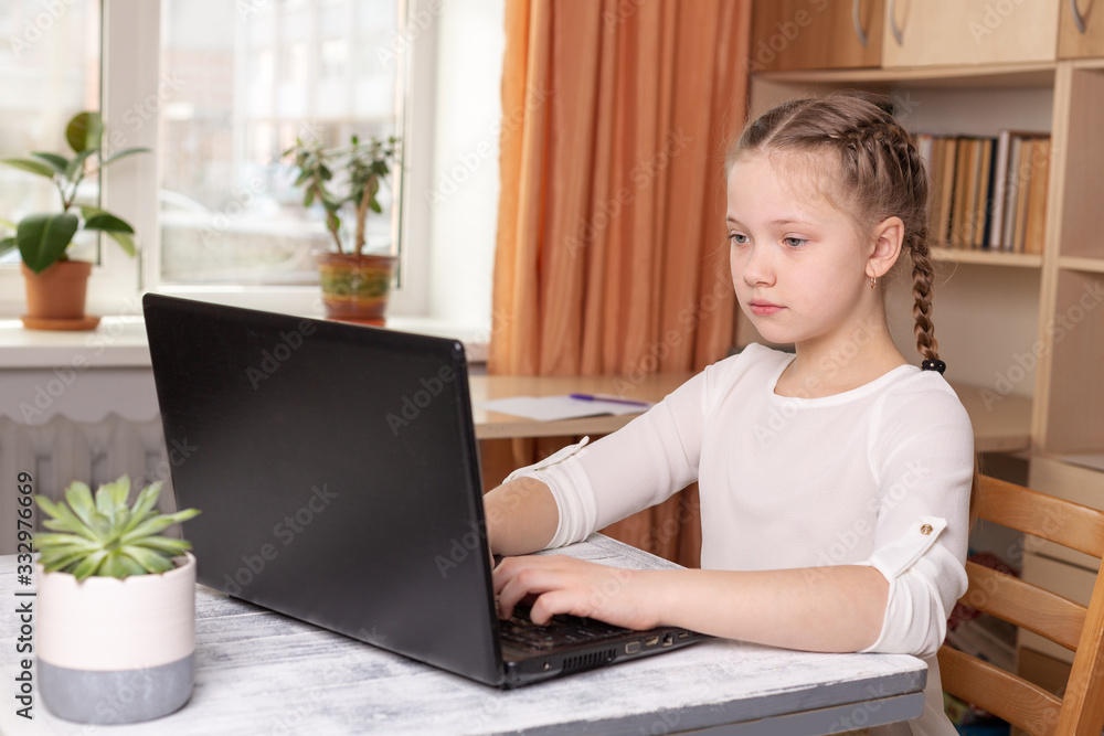 Serious schoolgirl working on a laptop. Distance learning online education, home school, home education, quarantine concept Serious schoolgirl working on a laptop. Distance learning online education, home school, home education, quarantine concept