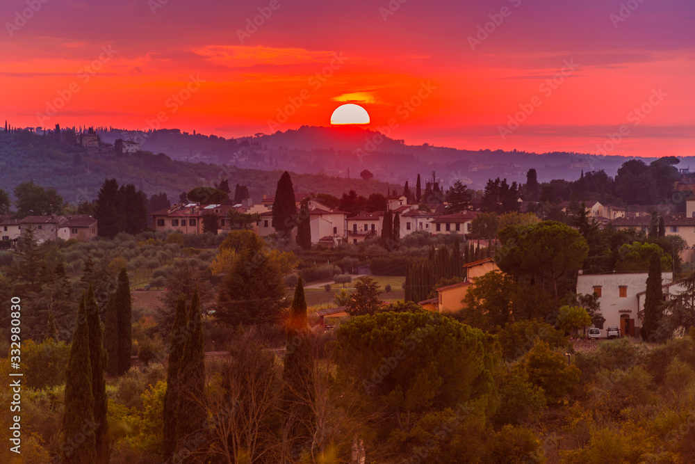 Classic Tuscan landscape with the warm sunset sun illuminating the green hills, cypresses, pines and villas