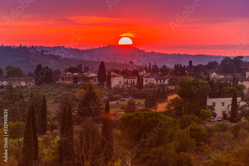 Classic Tuscan landscape with the warm sunset sun illuminating the green hills, cypresses, pines and villas