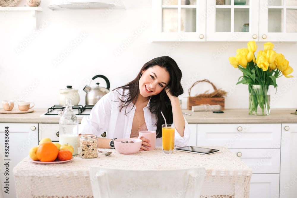 Young beautiful woman using digital tablet while breakfast in kitchen.