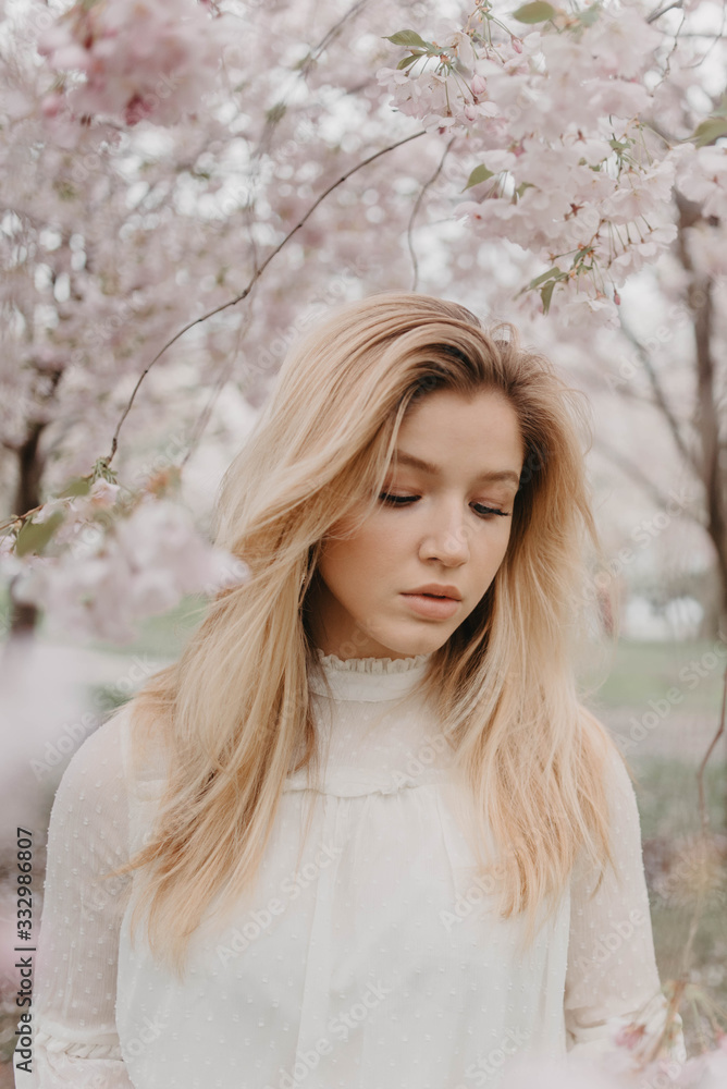 A young blonde woman standing amongst the cherry blossom trees A young blonde woman standing amongst the cherry blossom trees