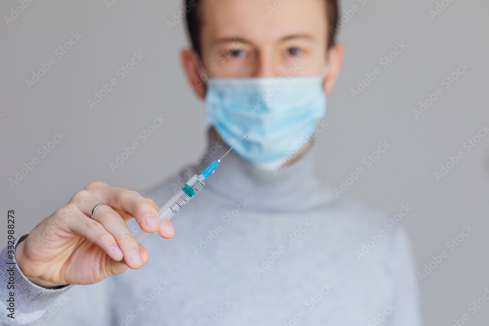 male medical worker in a mask holding a syringe, close up hand with a syringe on a background of blurred man male medical worker in a mask holding a syringe, close up hand with a syringe on a background of blurred man