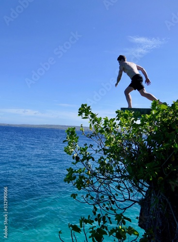 Man jumping from cliff into ocean, in air before blue sky, Siquijor, Philippines