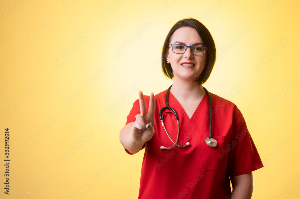 Beautiful woman doctor with stethoscope, wearing red scrubs showing victory Beautiful woman doctor with stethoscope, wearing red scrubs showing victory