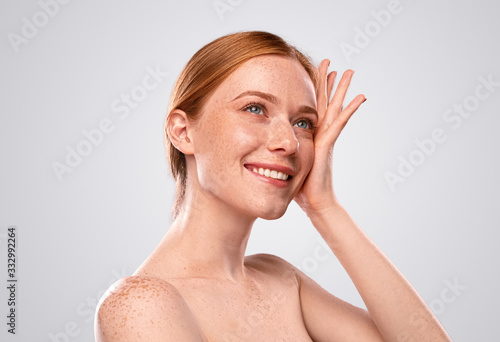 Charming redhead female with naked shoulders on gray background