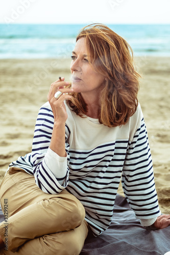 Portrait of a attractive woman of fifty years smoking at the beach photo