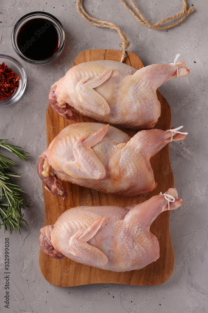Three fresh raw organic quails on wooden board on a gray background, Closeup, Top view