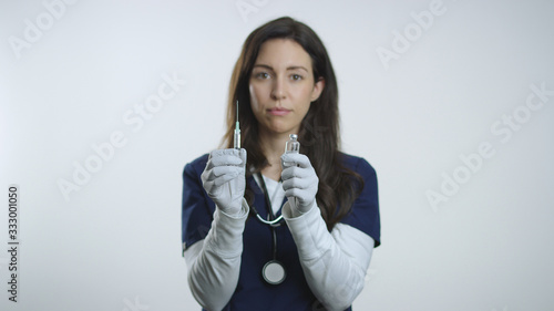 Brunette nurse holds up needle and vial after filling syringe with medicine © Jared