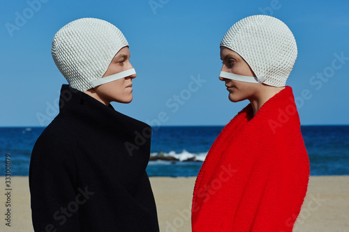Conceptual portrait of women wearing bathing cap standing on beach