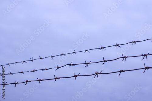 Barbed wire on fence on a background of blue clouds, protected object, no trespassing