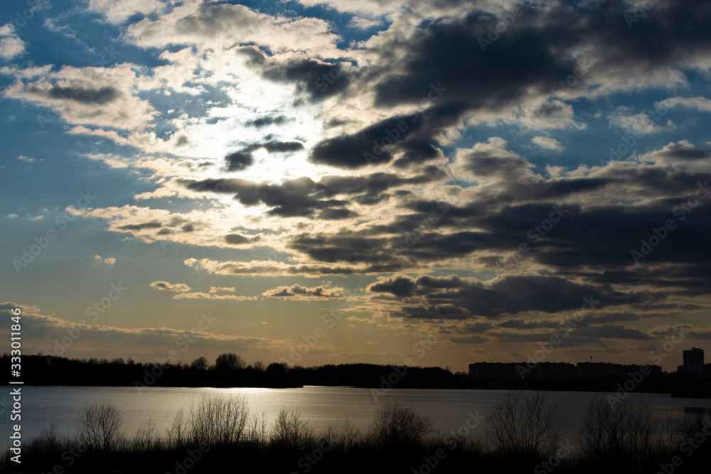 Thick clouds are lit by the sun at sunset. Blue sky and bright sunset sun. Thick clouds are lit by the sun at sunset. Blue sky and bright sunset sun.