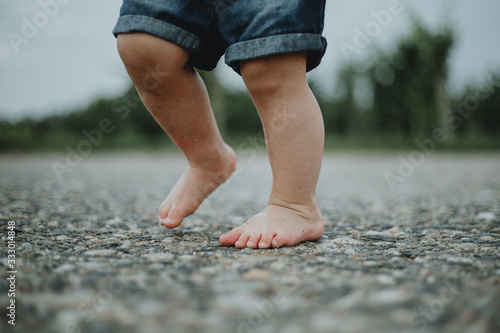 Little kid's dirty feet stepping on the ground, wearing denim shorts taken from the low angle
