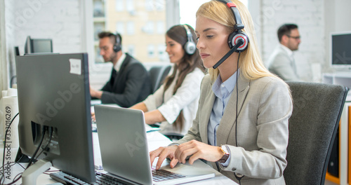 Female telephone worker in headset working on laptop in office