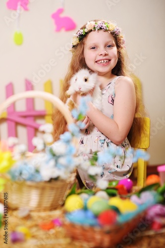 child-a little girl in a dress and a flower wreath on her head smiling and holding an Easter Bunny on the background of flowers and decor