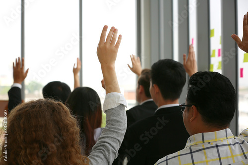 Real view of curious business people raising hand at multiracial group meeting engaging in offered activity, business event or asking question at corporate business training, seminar or workshop