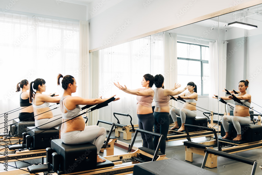 Pregnant woman practicing pilates with equipment reformer Pregnant woman practicing pilates with equipment reformer