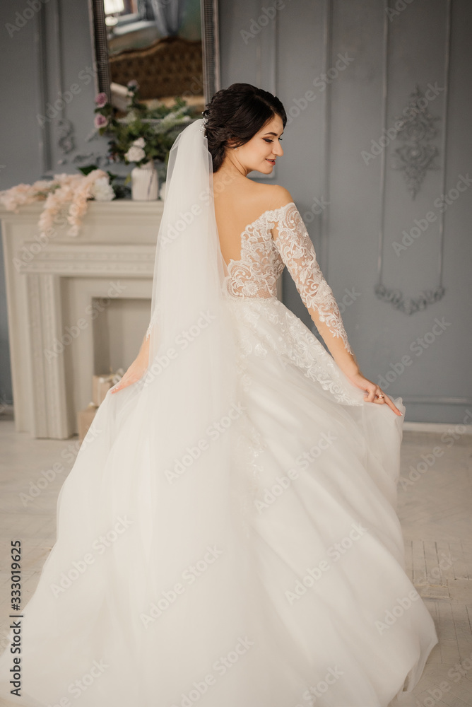 Elegant young bride holds wedding dress with hands, smiling looks away. Full-length portrait of a bride in a vintage interior. Beautiful bride portrait. Elegant young bride holds wedding dress with hands, smiling looks away. Full-length portrait of a bride in a vintage interior. Beautiful bride portrait.