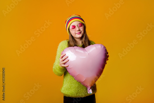 happy teenage girl in sunglasses holds a heart-shaped balloon