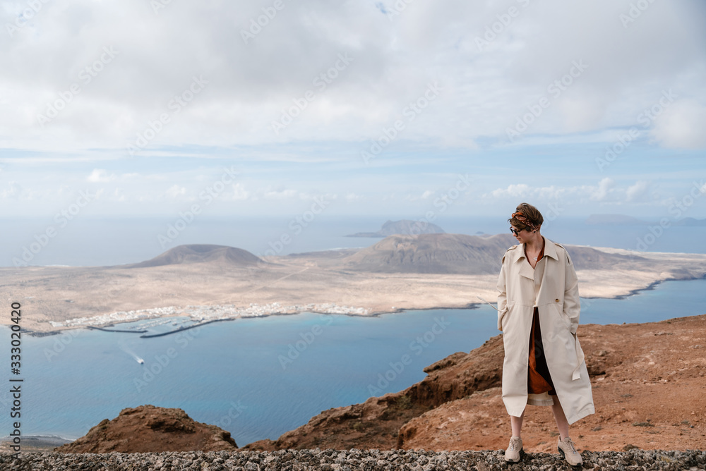 Woman in beige trench coat standing on high stone wall. Woman in beige trench coat standing on high stone wall.