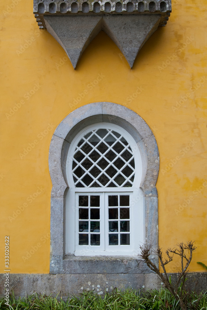 The yellow facade of the house. White window with bars and green grass under it.